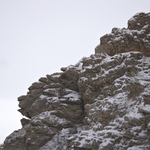 A rocky ledge with snow on it in a bright cloudy sky