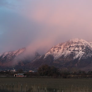 The snowy mountains are red with sunset, an asphalt road curves up into the distance bordered by brush and oaks