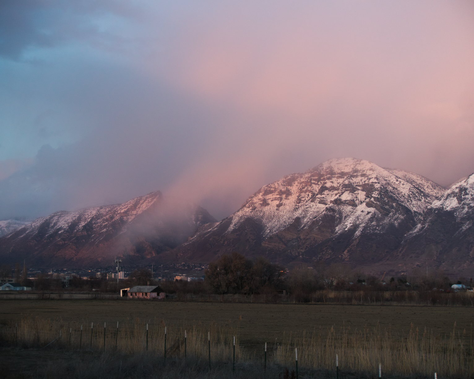 Above a field with an old barn in it, the mountains with some peachy, misty clouds