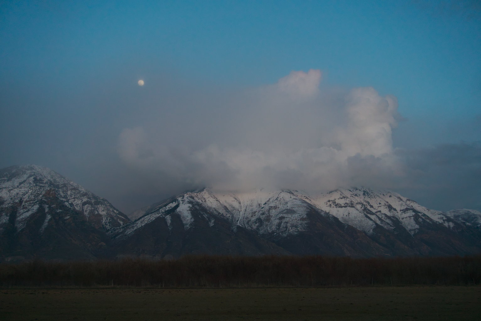 Snowy mountains topped with misty clouds, the nearly full moon hazy, peaking up out of the clouds