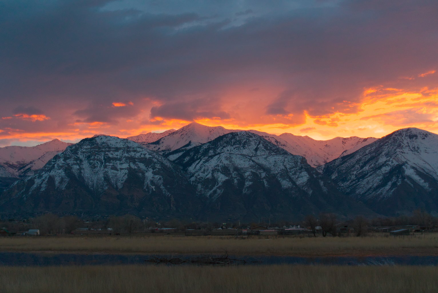 Snowy layered mountains with orange glowing clouds above, the snowy peaks in the back are reflecting the orange light in the clouds