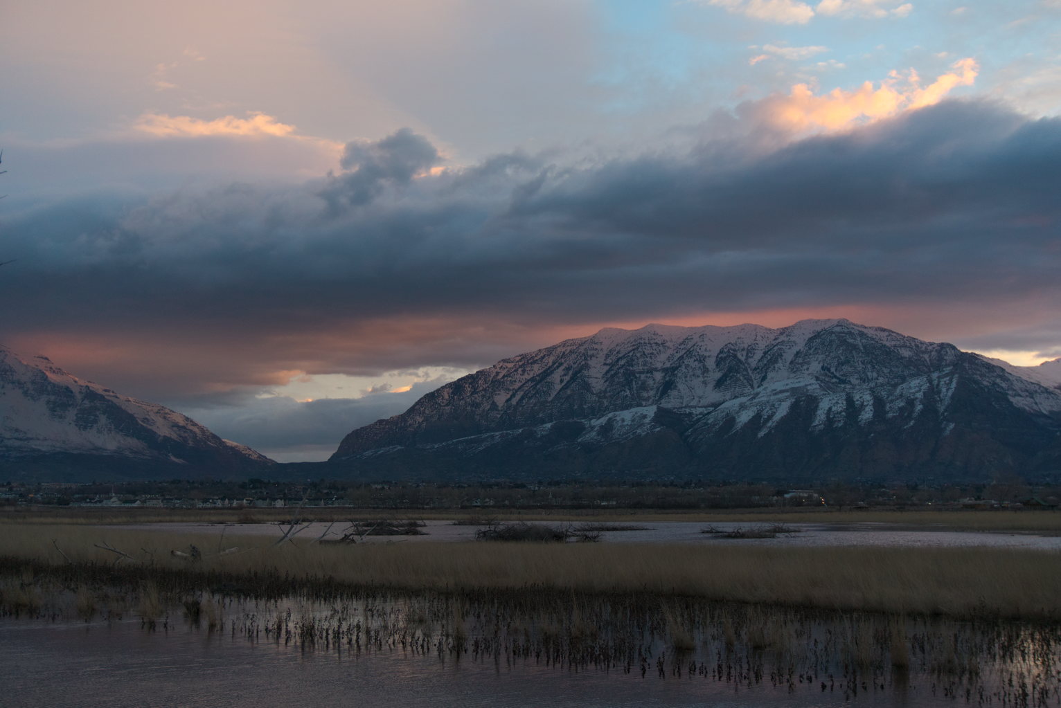Calm sunrise glow in clouds over snowy mountains, wetlands in the foreground