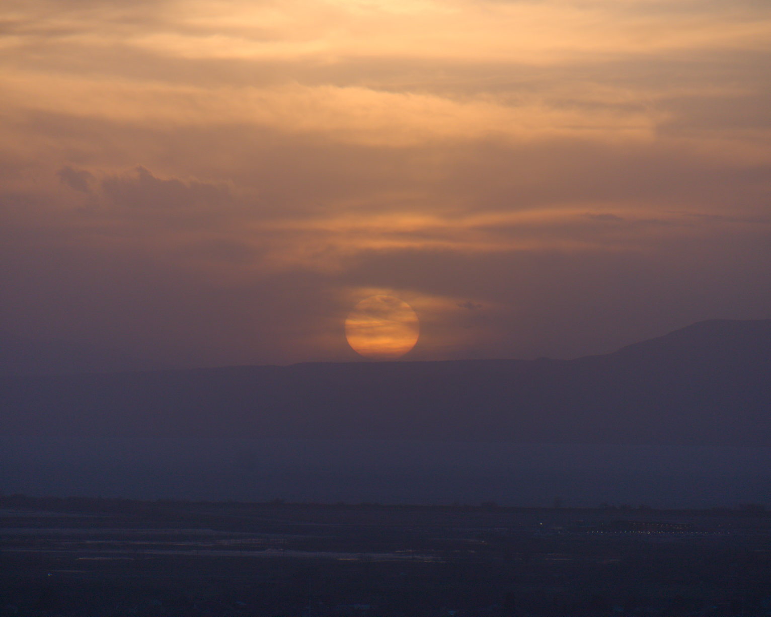 The circle of the just setting sun above the west mountains through a haze