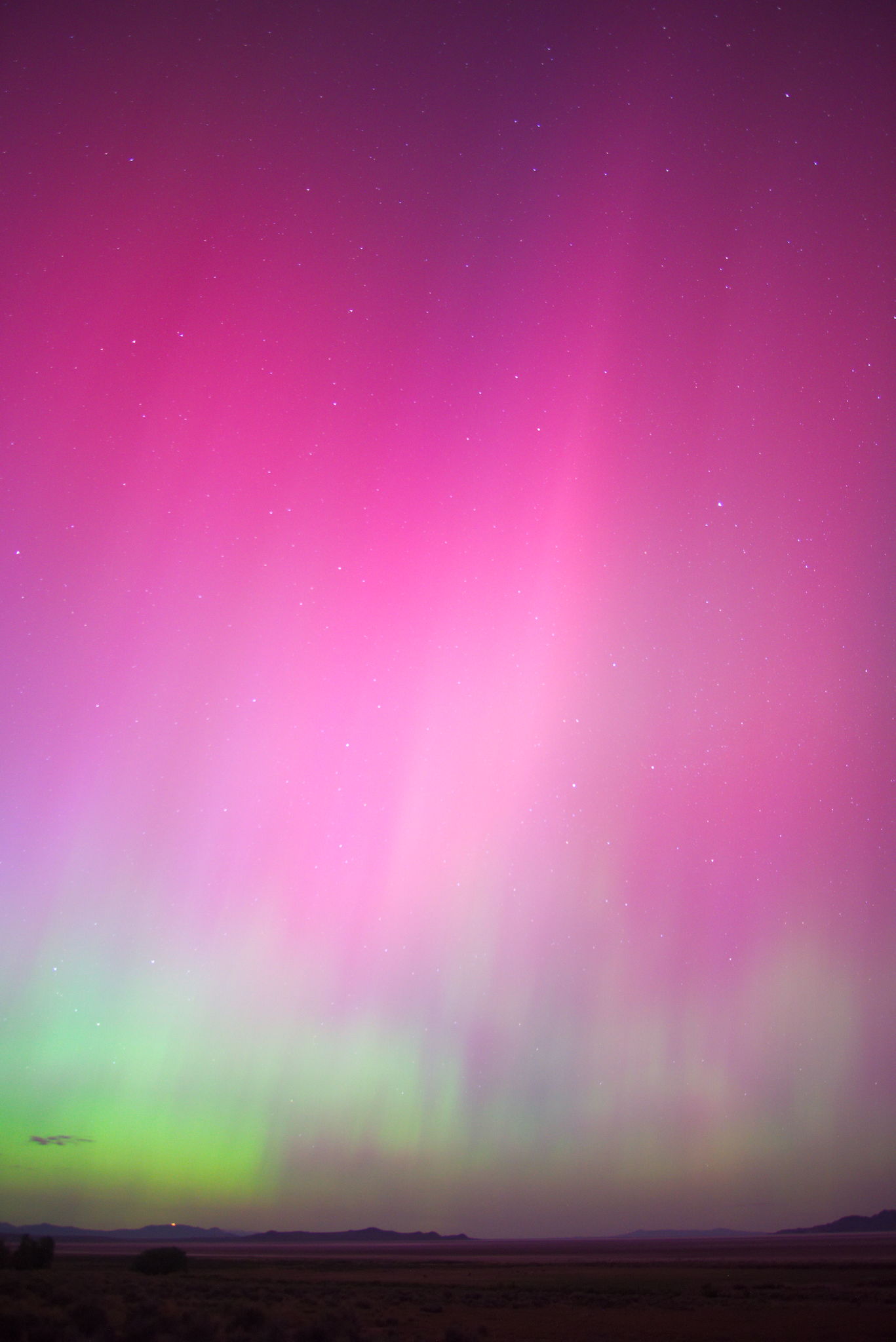 Green aurora dances lower on the horizon with lighter pillars rising into the pink wash above