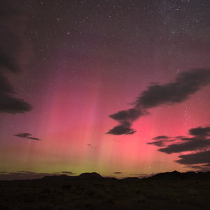 Bright aurora pillars glow magenta with some green color visible below over a rural landscape with some clouds.