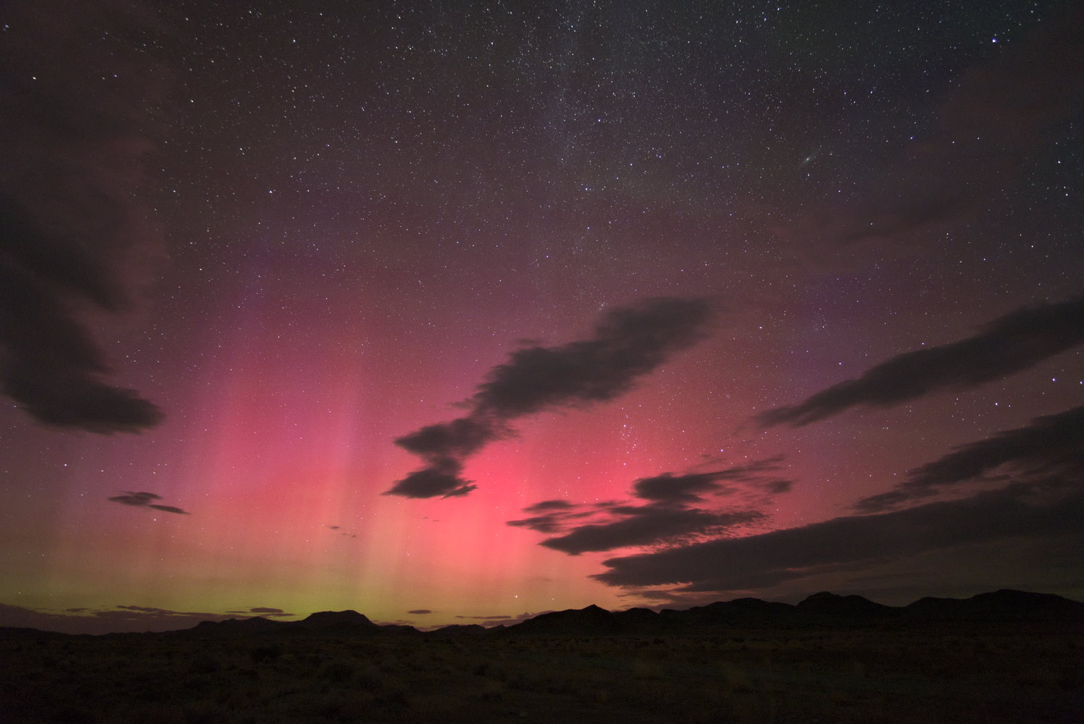 Bright aurora pillars glow magenta with some green color visible below over a rural landscape with some clouds.