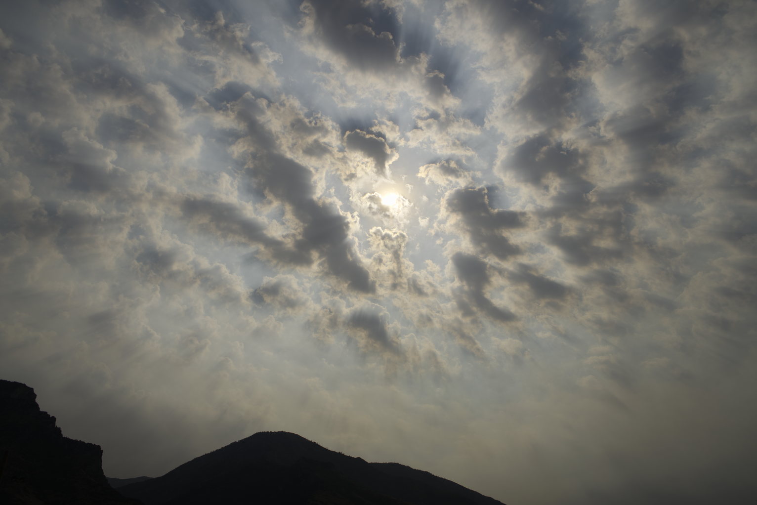 The partly cloudy sky is hazy with smoke casting ray shadows that emminate from the sun in the middle of the photo