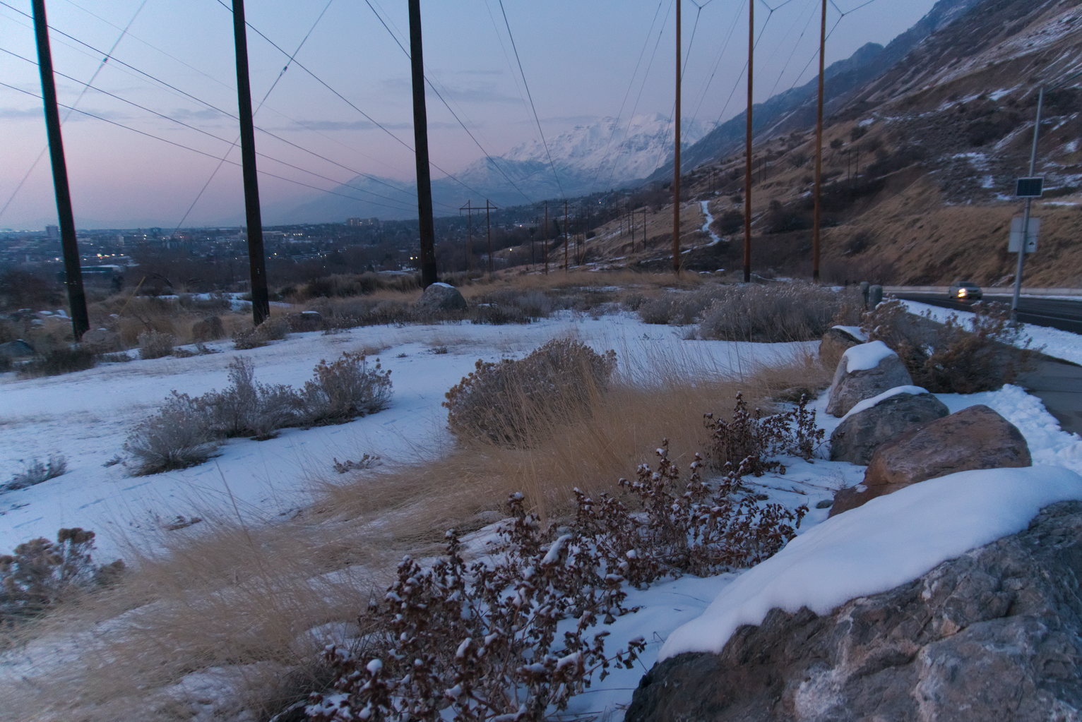 Dry grasses, snow, and sage, in the distance town and behind that mountains