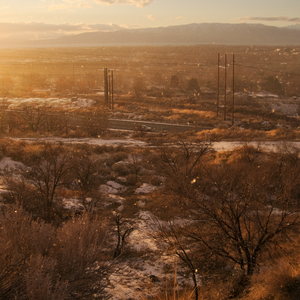 Snow whirls around in front of the mountainside below with trees and town and mountains in the distance