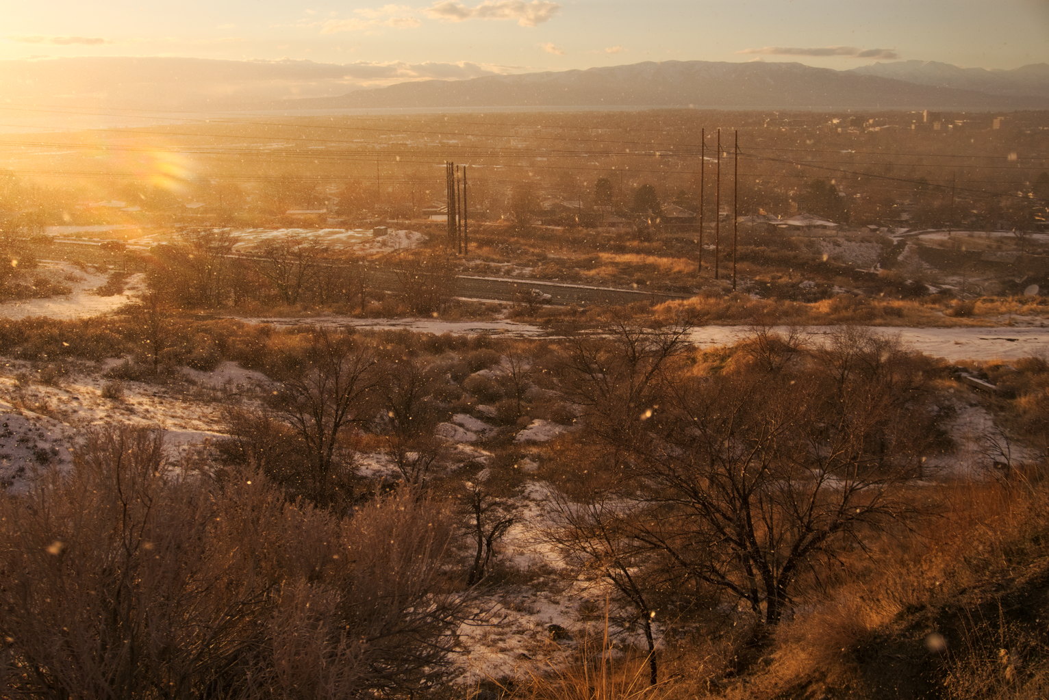 Snow whirls around in front of the mountainside below with trees and town and mountains in the distance
