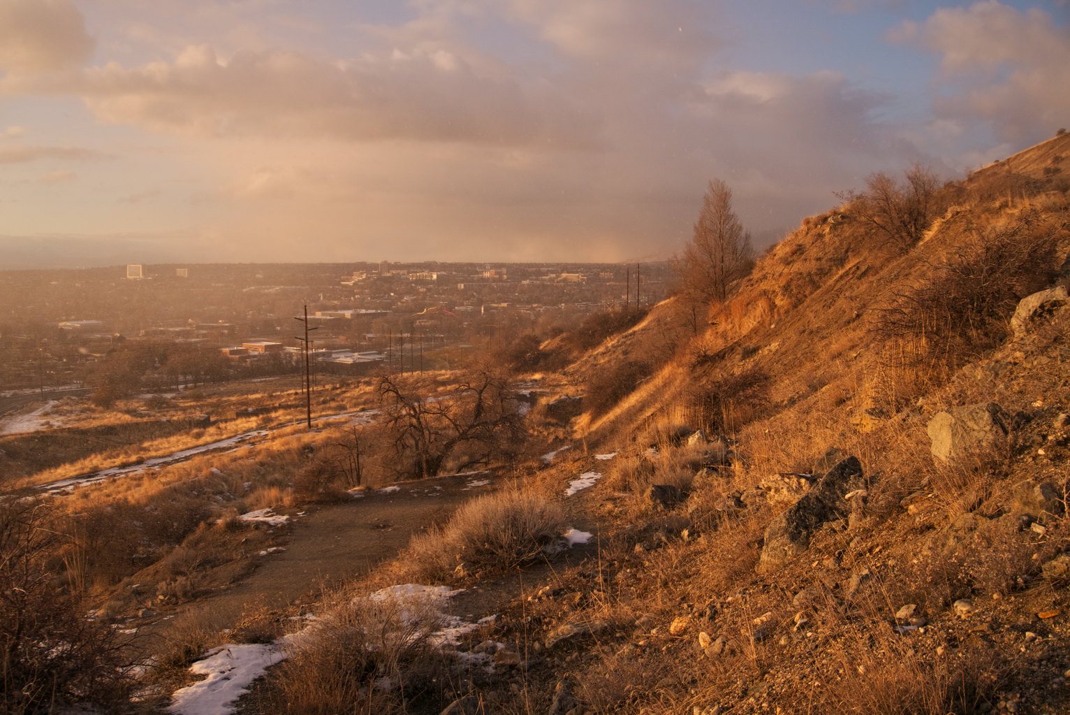 Sunlight hits the mountainside, snowfall visible in the distance out over the town.