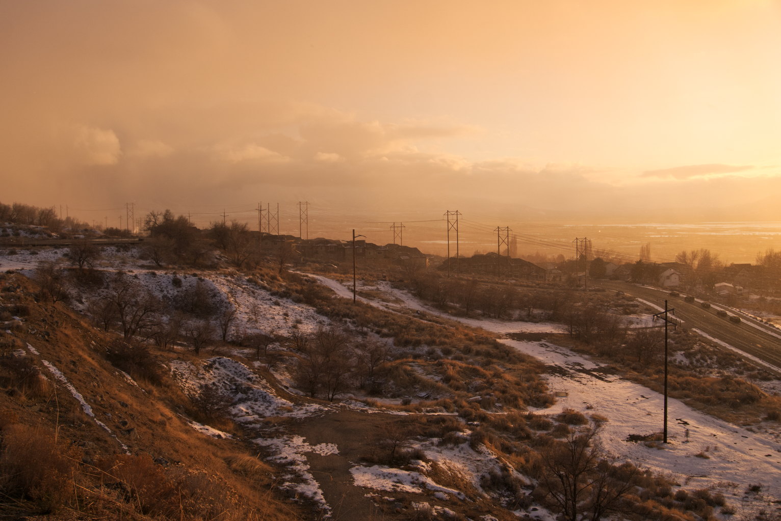 Golden mountainside with some snowfall, power lines.