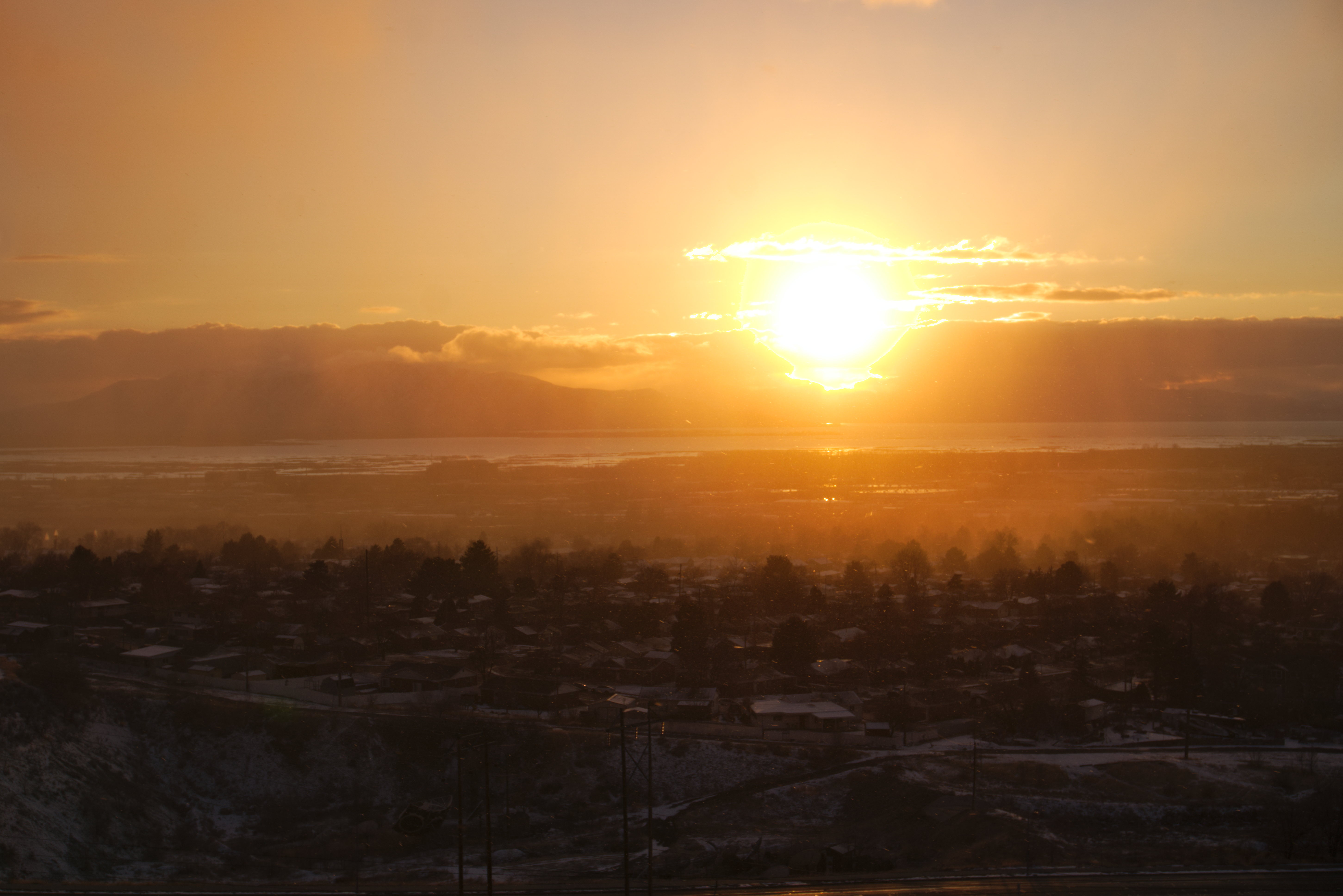 The hazy edge of a snowfall makes a line across town, sun almost setting below the low clouds.