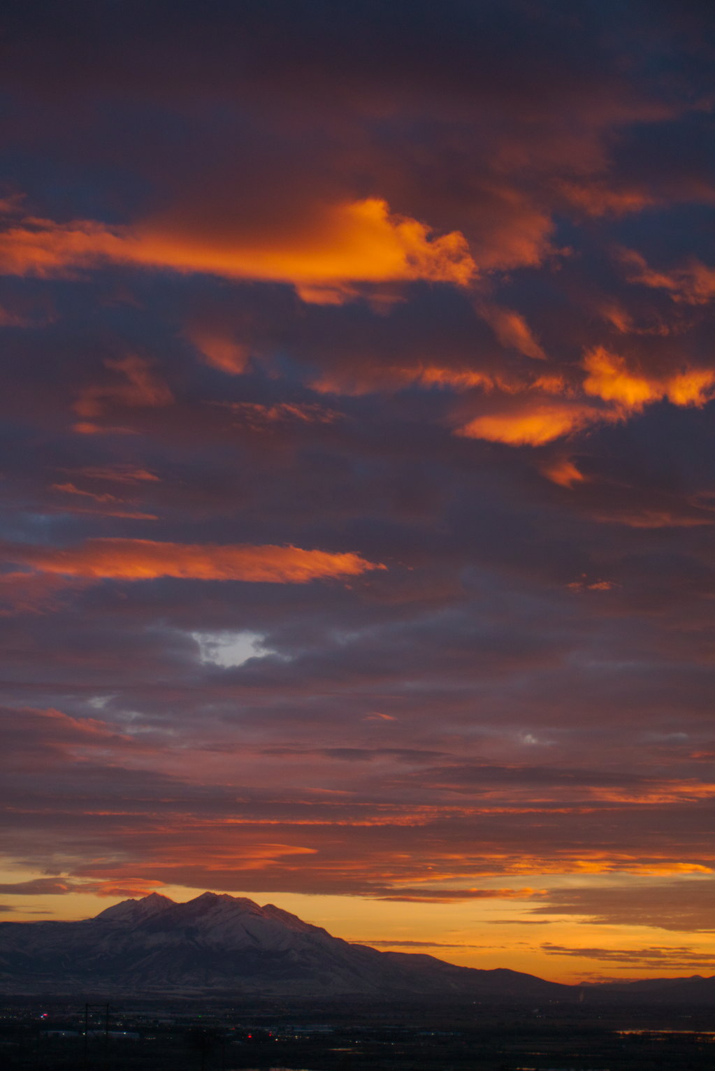 The undersides of grey-blue clouds lit bright orange by the set sun, the snowy mountain in the distance over town glows faintly orange