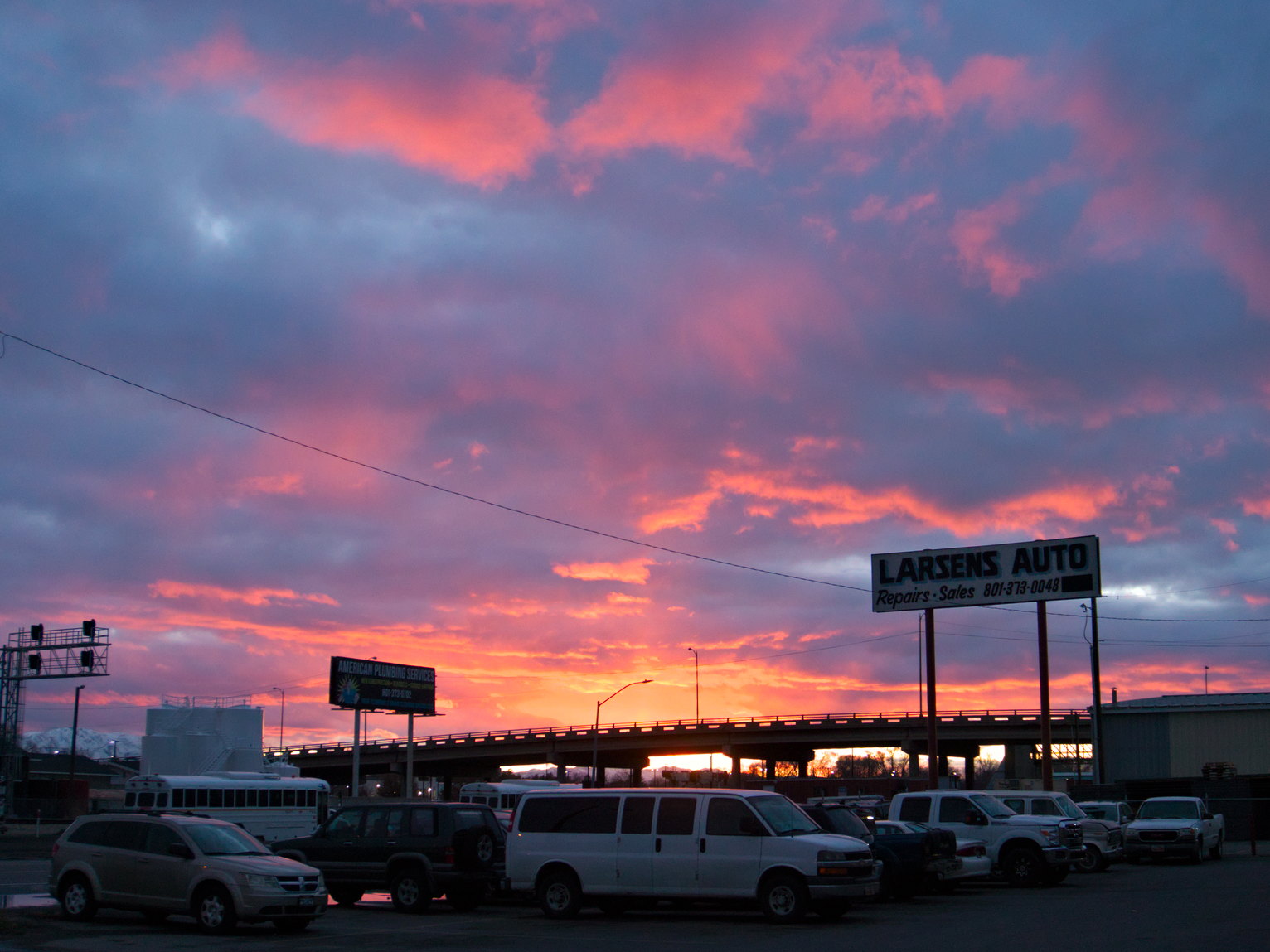 The underside of blue/grey clouds lit orange by sunset over a parking lot