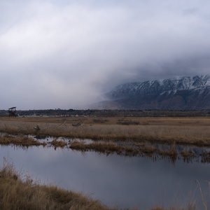 A still creek in dry grasses reflects the bright snowy storm coming in from the north hiding the mountains