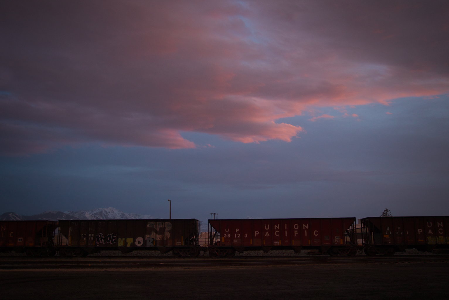 Cloud cast red in sunset against darker blue ones above train cars.