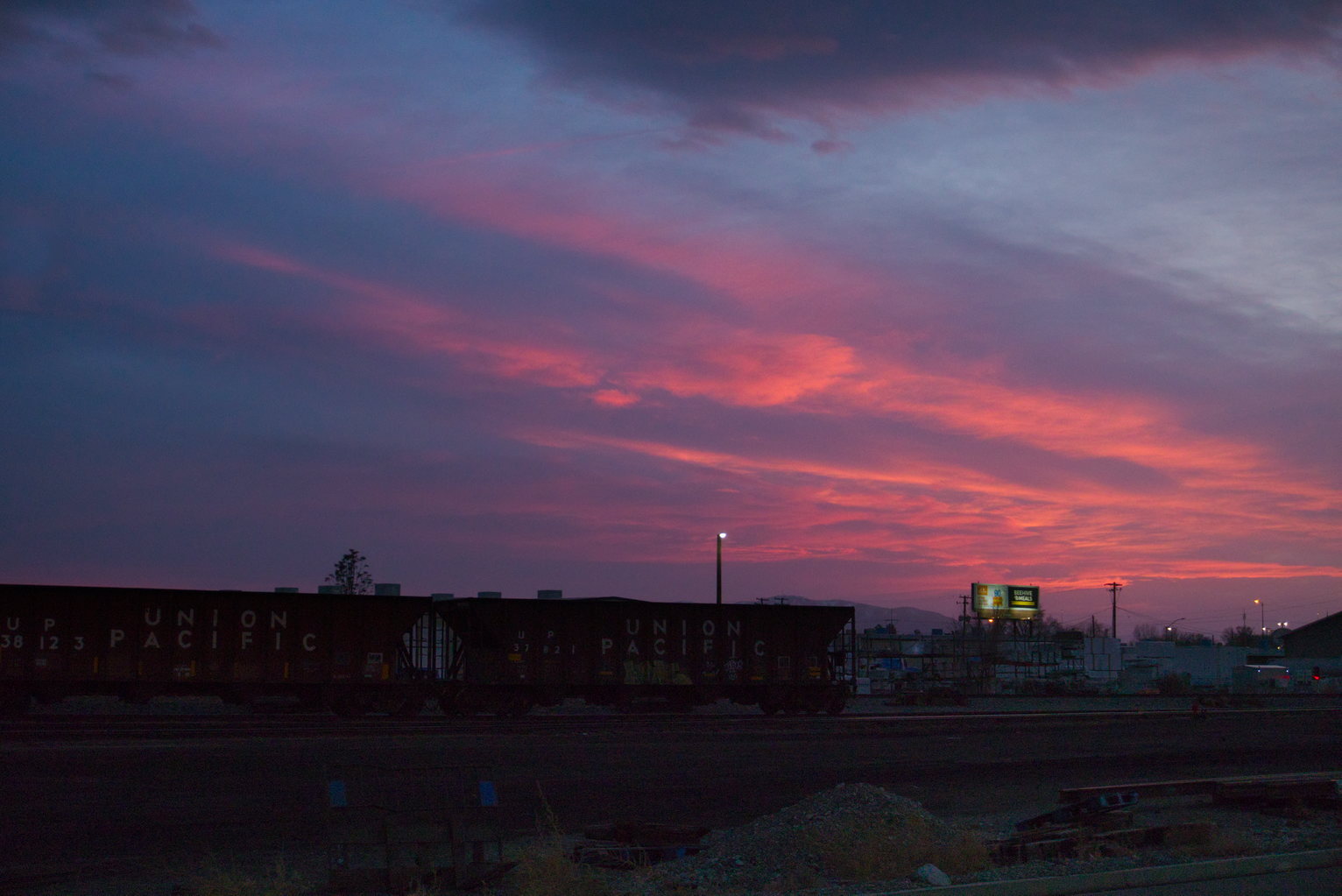 Magenta streaks of color in the clouds from a deepening sunset over train cars.