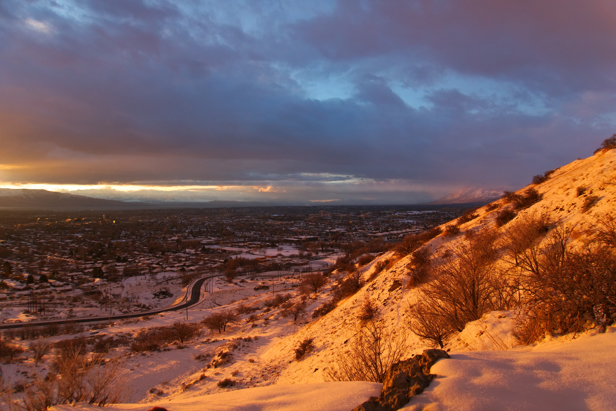 Looking down from a snowy mountainside at a town bathed in strong sunset light