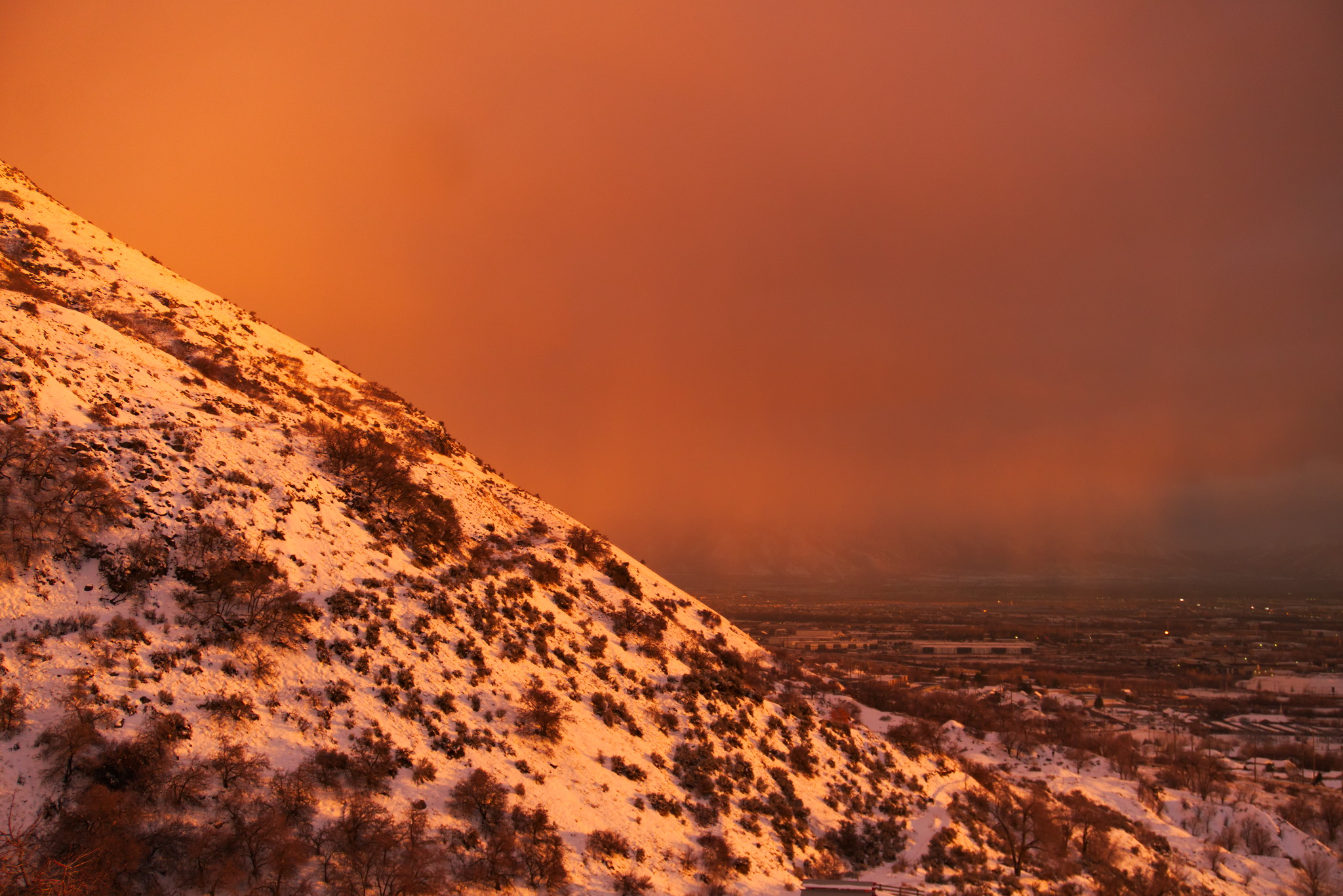 Looking at the neighboring snowy foothill dotted with scrub oak and sage brush bathed in strong sunset light with a red glowing misty sky above