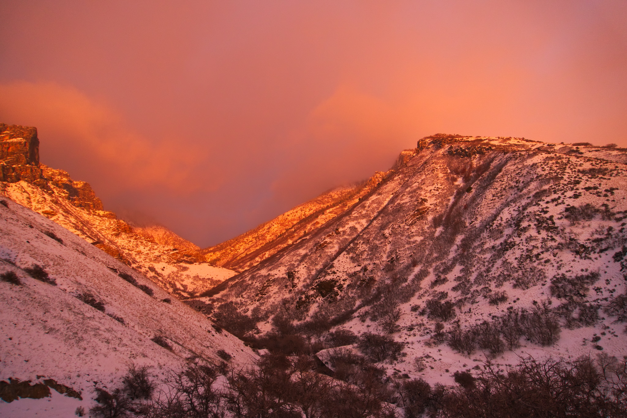 Looking up at the mountain peaks rocky and dotted with scrub, the higher parts bathed in strong red sunset light