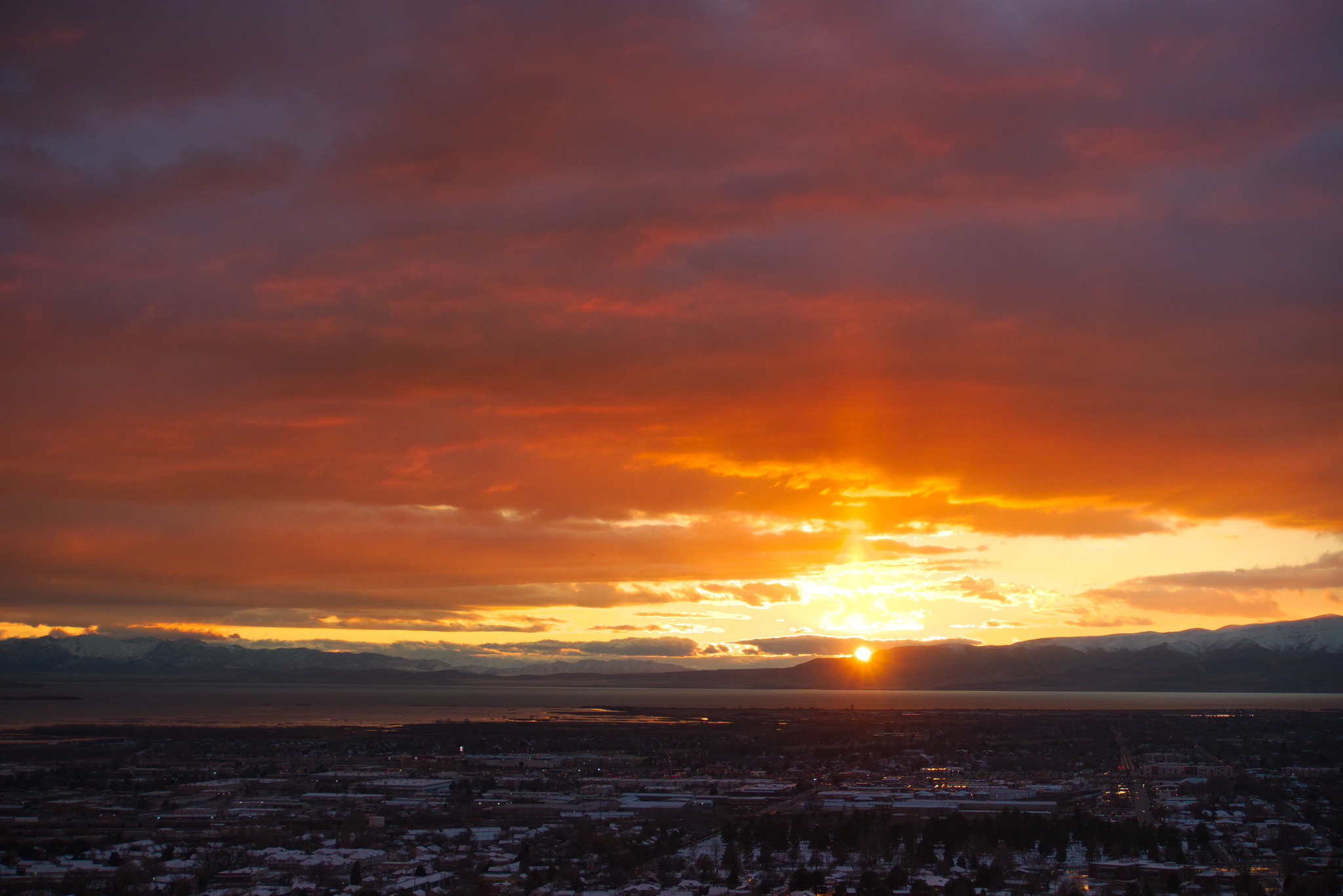 Looking out over town beyond which the sun is partly set over the mountains, the clouds in the sky aglow