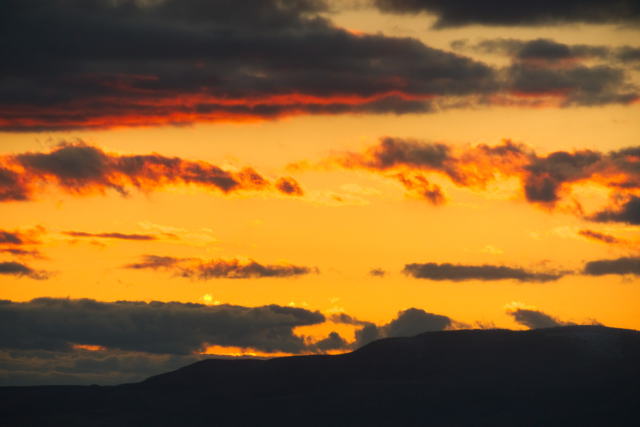 A close look at the glowing clouds just above the far mountains in sunset yellow sky