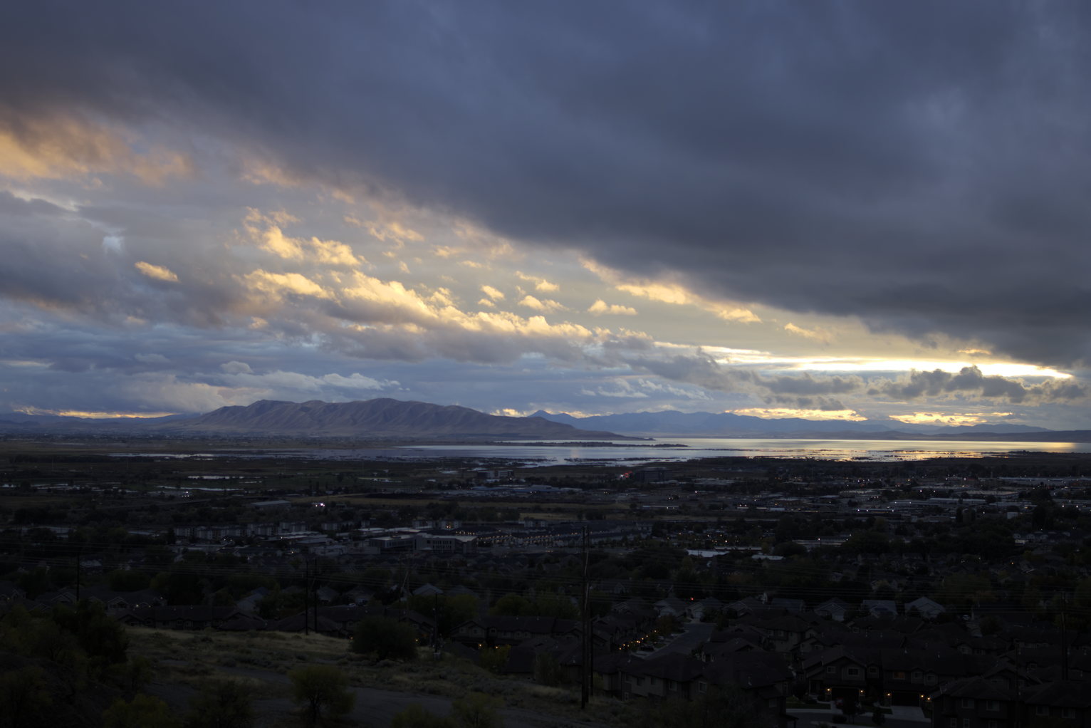 The falling sun lights a diagonal swash of clouds a peach color above the mountains, lake, and town