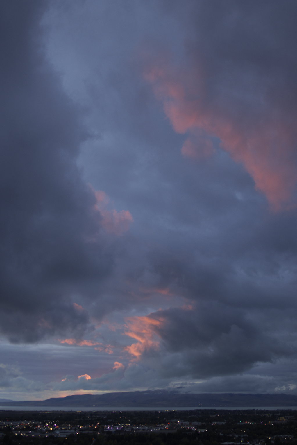 In the cloudy deep blue sky the edges of some clouds glow red above the lake and mountains, above the scattered town lights
