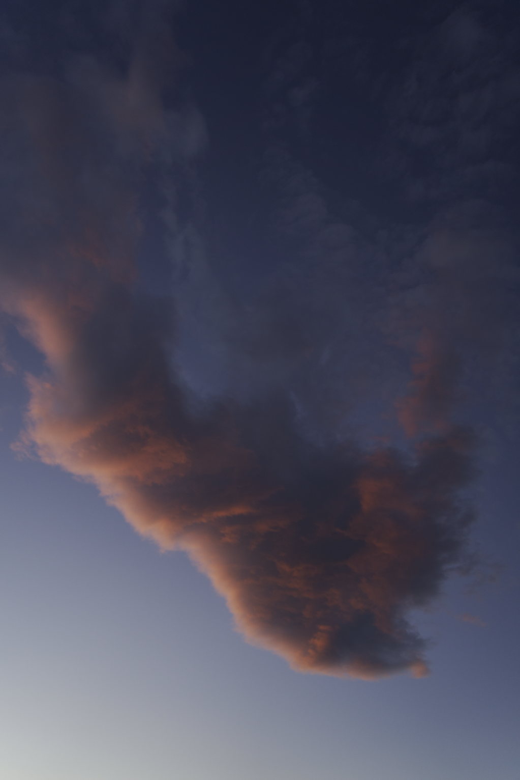 Dramatic twilight clouds tinted pink and orange against deep blue sky, the clouds forming sweeping shapes as they catch the last light of day