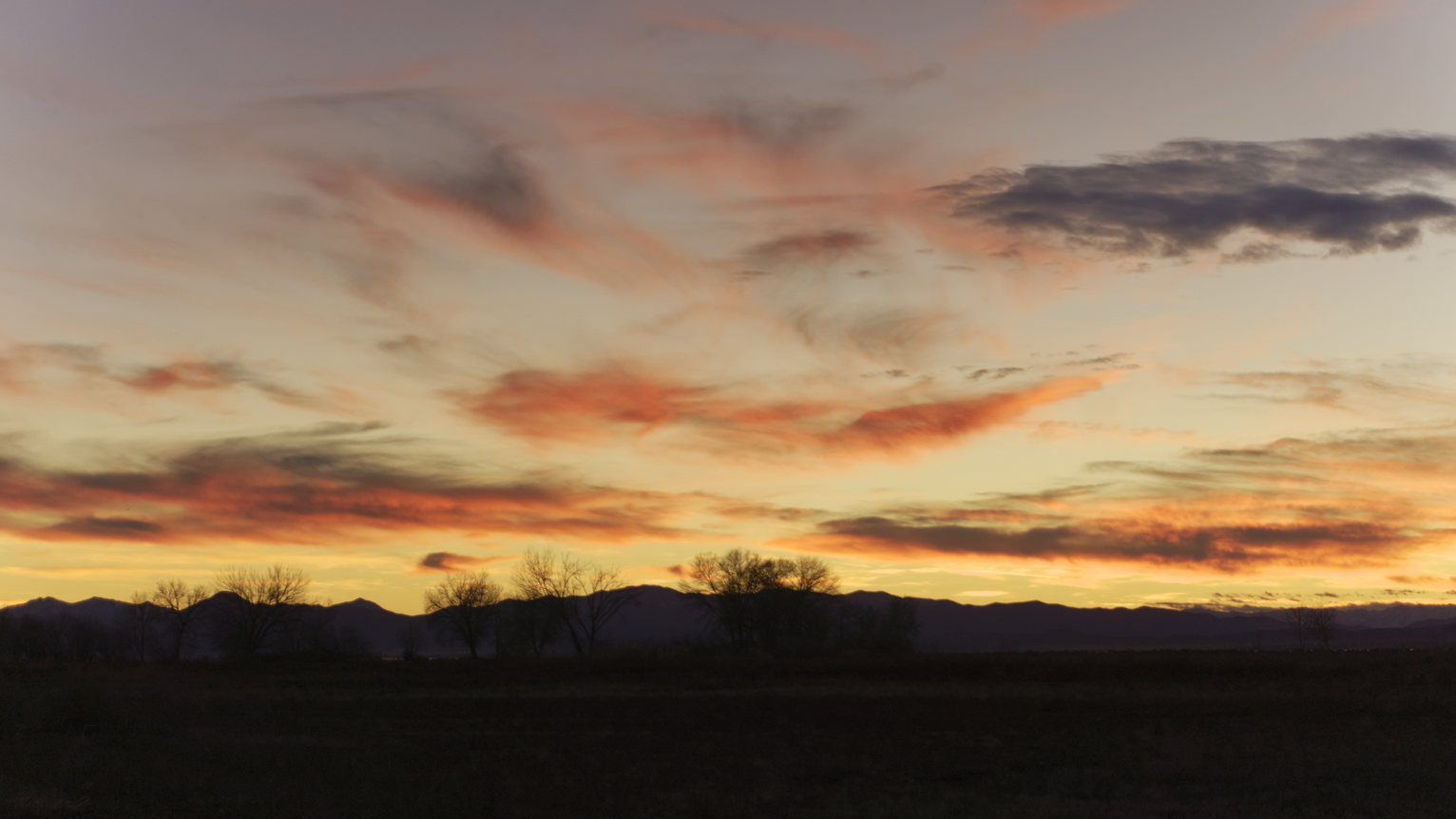 Red and orange clouds above silhouetted bare trees and mountains