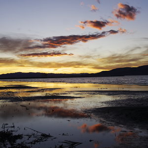 Orange and pink clouds reflected in shallow water at sunset with silhouetted mountains