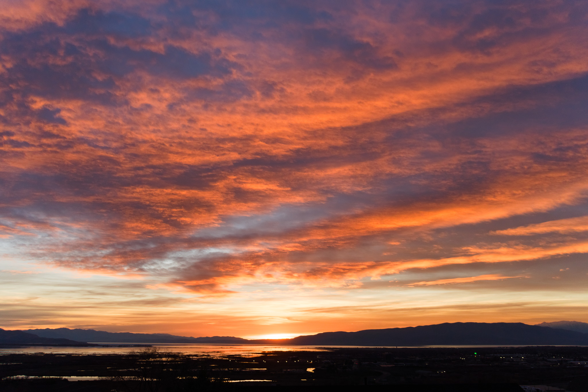 Clouds high up into the sky glow in sunset over a distant mountainside and a lake