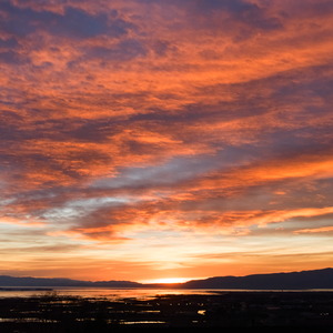 Clouds high up into the sky glow in sunset over a distant mountainside and a lake