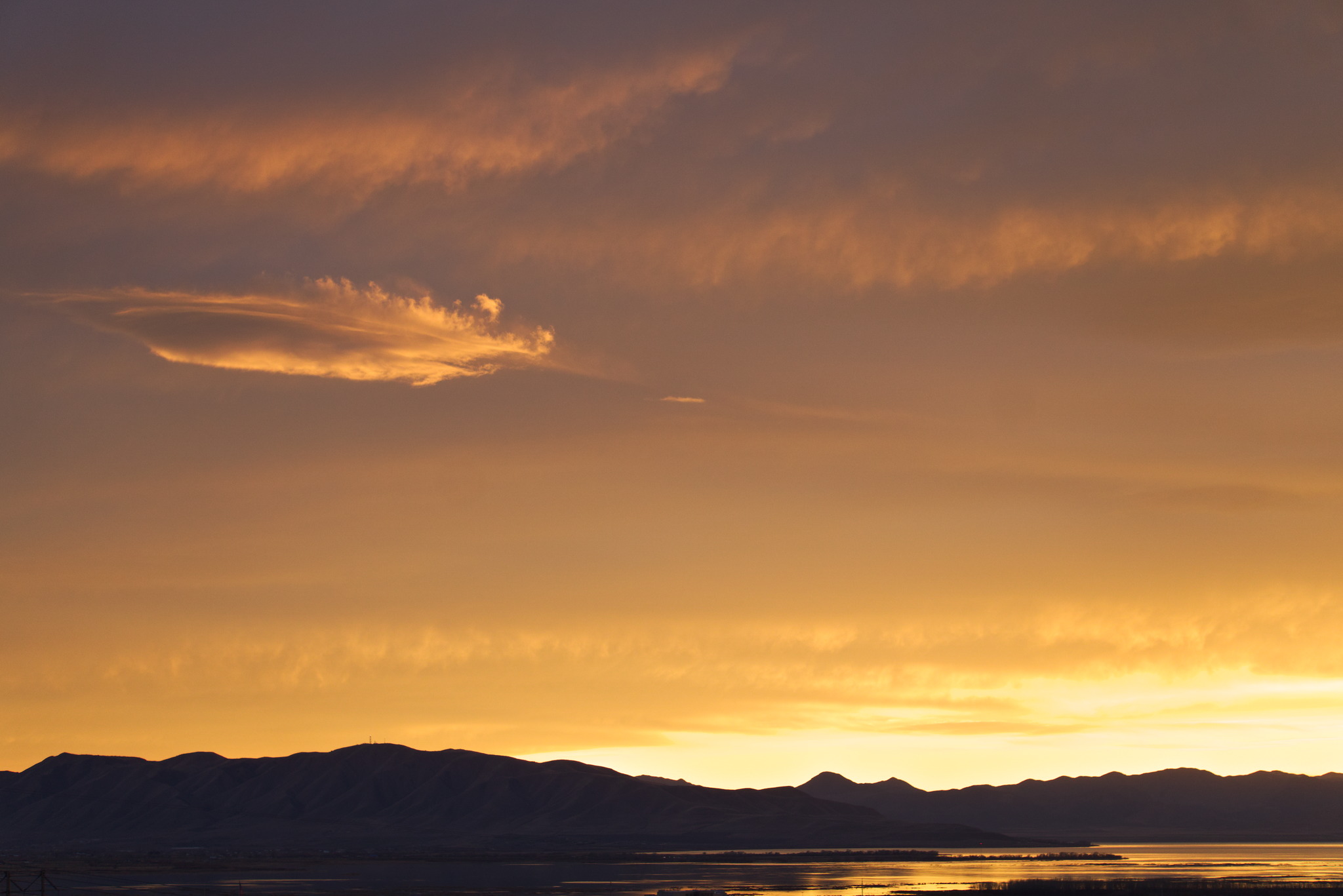 Clouds orange and purple grey from sunset above distant mountains and a lake reflecting the orange