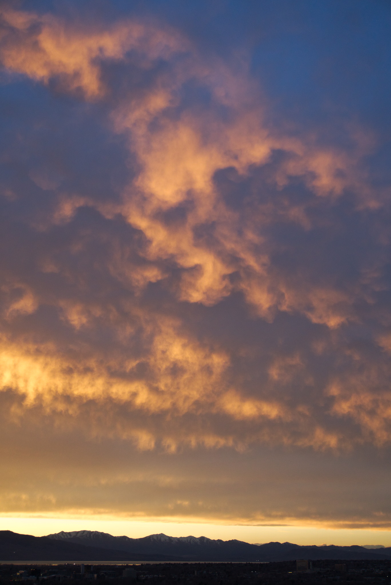 High above the distant mountains clouds catch orange sunlight in a bubbly pattern against darker clouds and above deep dusk sky