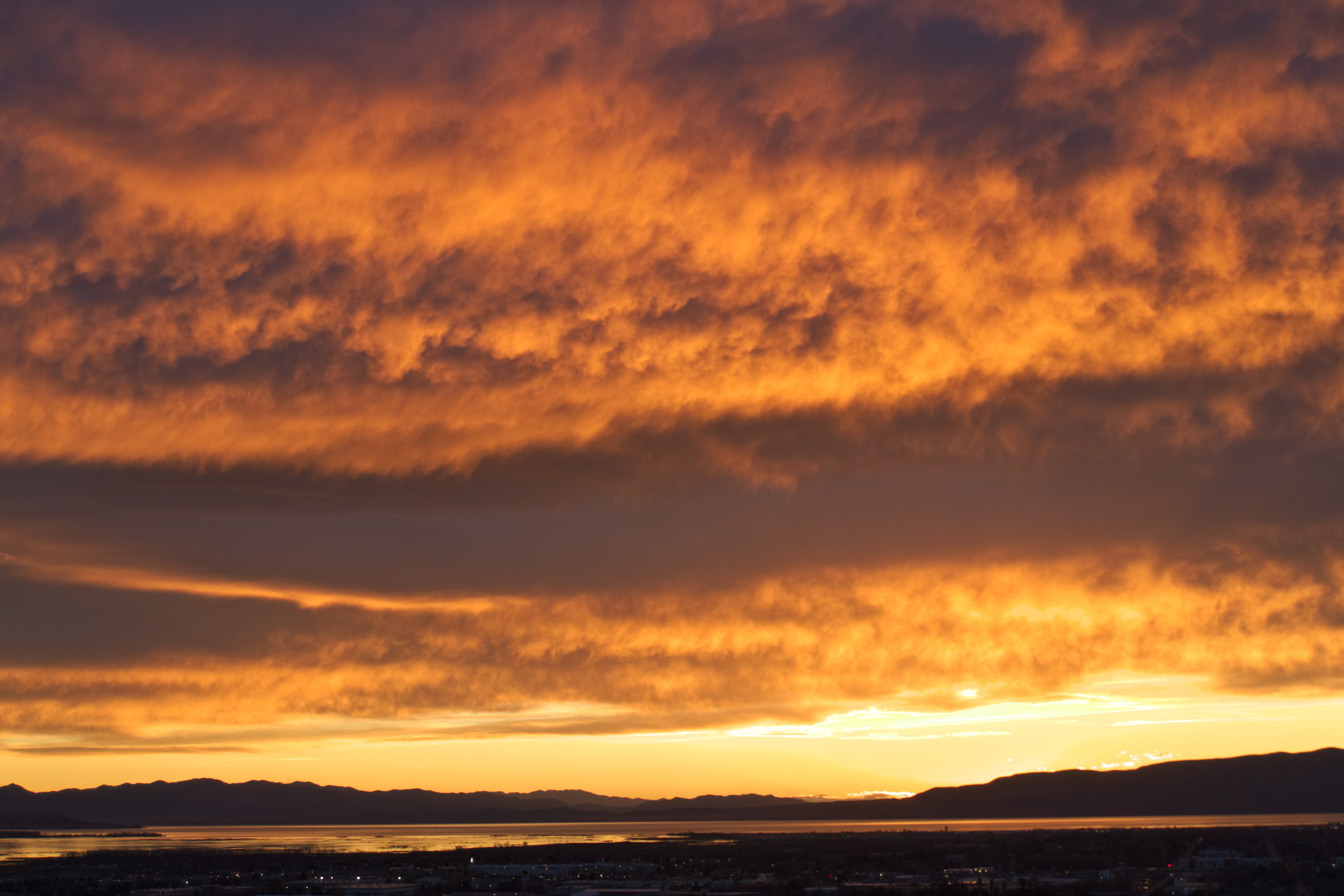 Clouds dramatically catch orange light in a spectacular sunset over town, the lake, and distance mountains