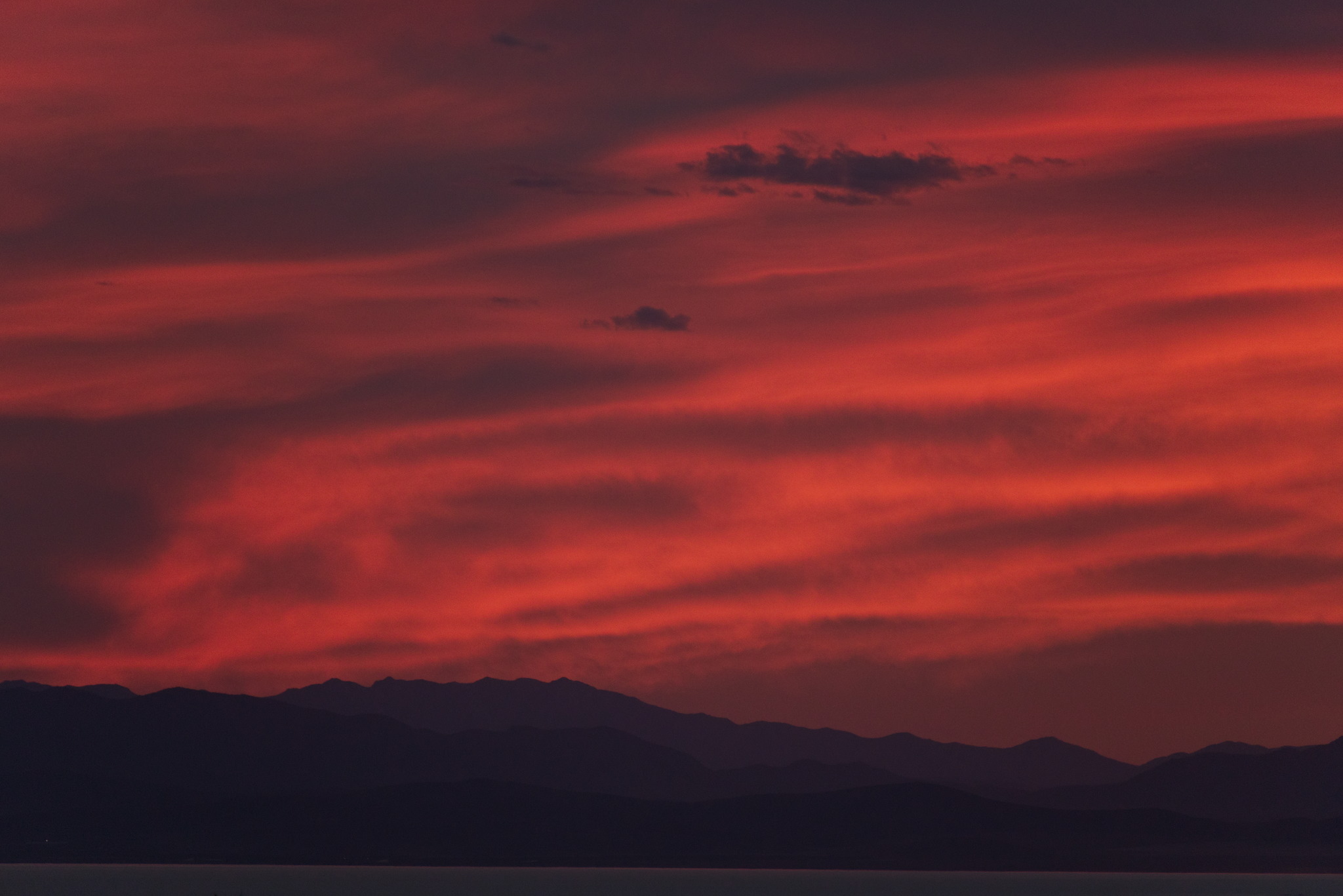Swirls of orange lit clouds over three layers of distant mountain ranges