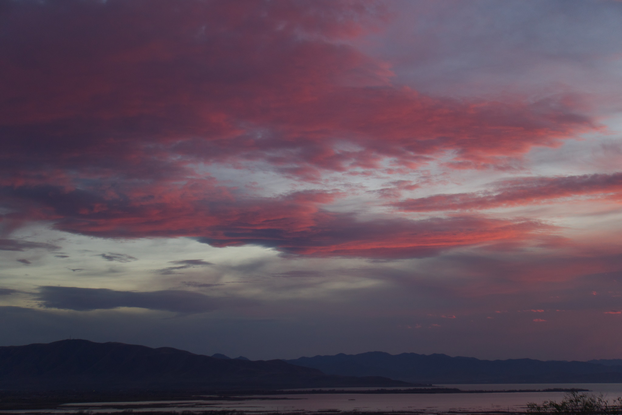 Above a lake and some distant mountains grey clouds at dusk begin to turn orangey pink