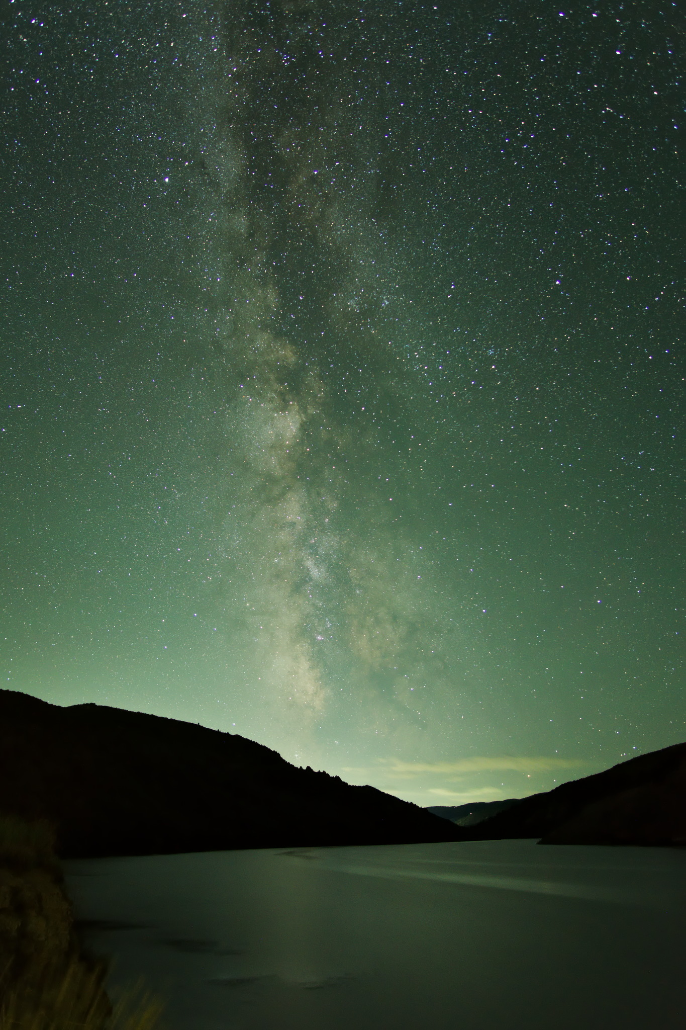 A closer view of the first nightscape where the milky way rises into a greenish sky above a river glowing with the same greenish light