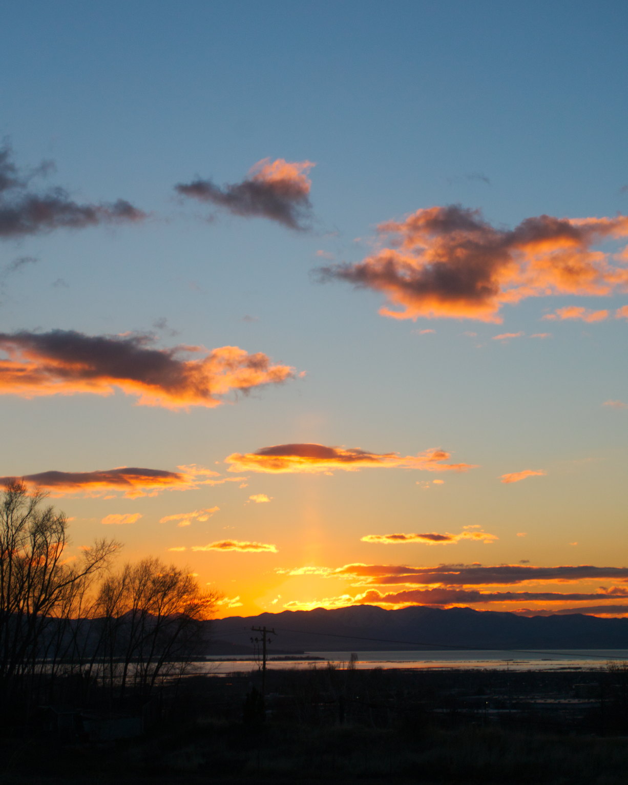 A sun pillar stretches up over the mountains into the orange sky, orange clouds