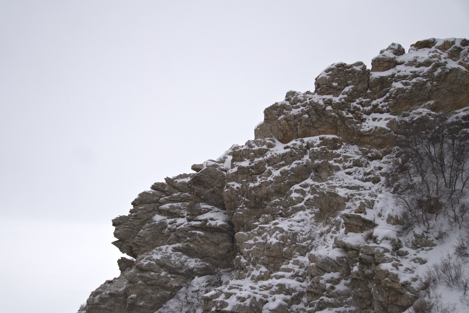 A rocky ledge with snow on it in a bright cloudy sky