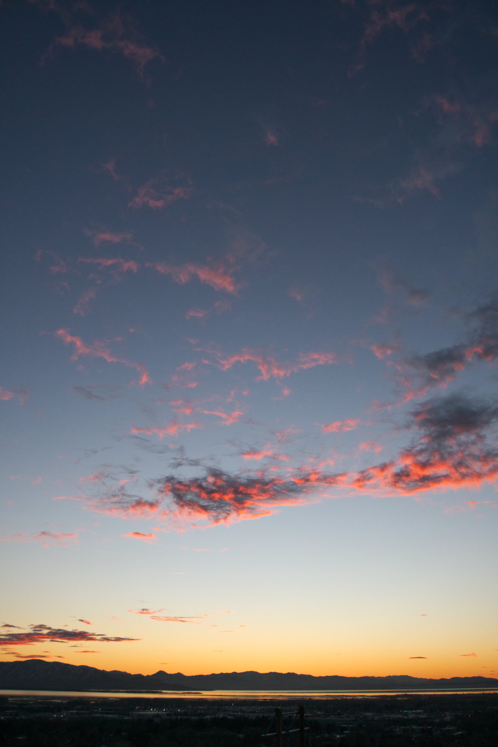 Whispy clouds out west catch bright orange sunset light in a sky going from yellow to turquoise to blue.