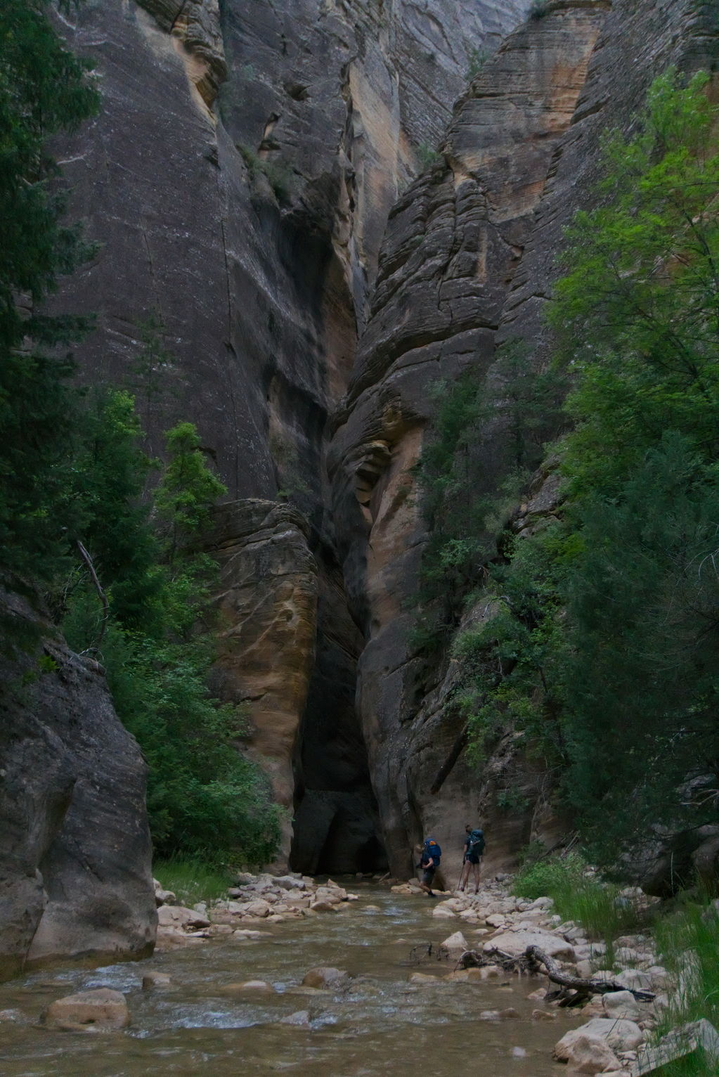 Two backpackers lower themselves into the water to continue on through the slot