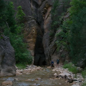 Two backpackers lower themselves into the water to continue on through the slot